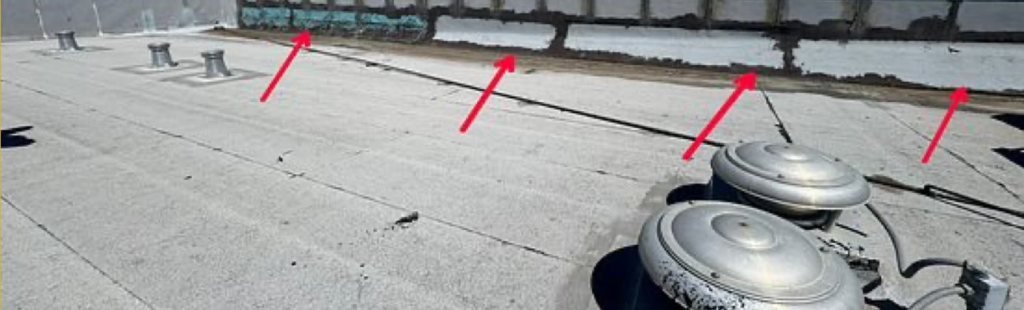 Commercial flat roof in Marysville with failed earlier patches along the wall transition where water was leaking inside, marked with arrows