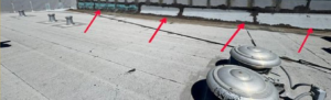 Commercial flat roof in Marysville with failed earlier patches along the wall transition where water was leaking inside, marked with arrows