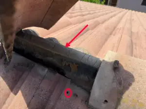 Worn, peeling flash band under a tile ridge on a Rocklin roof, with an exposed nail hole circled in the top row of tile