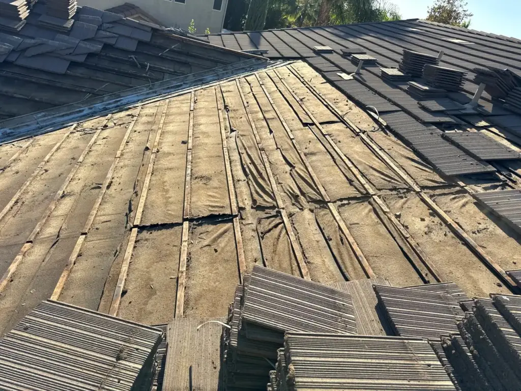 Tiles lifted on a Roseville tile roof showing worn, torn felt underlayment in the valley and field